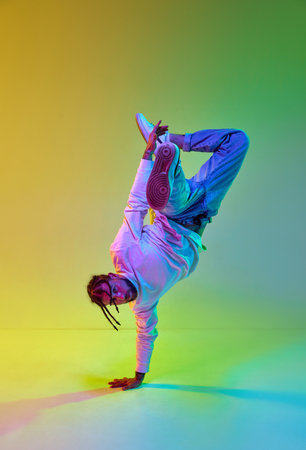 Young sportive guy with dreads hairstyle dancing hip-hop, breakdance against gradient yellow green...