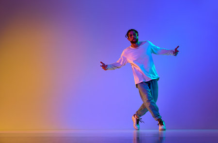 Dance show. Young guy dancing contemp, breakdance and hip-hop against gradient multicolored studio background in neon light. Concept of street style dance, fashion, youth, hobby, dynamics, adの写真素材