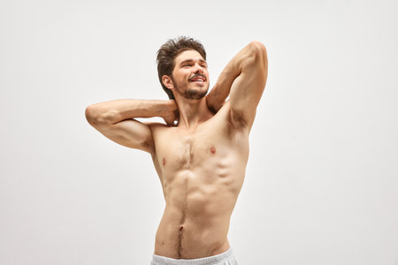 Smiling handsome young dark-haired man posing and showing his muscled body isolated over studio background. Male natural beauty. Concept of mens health, posing, beauty, body and skin care.の写真素材