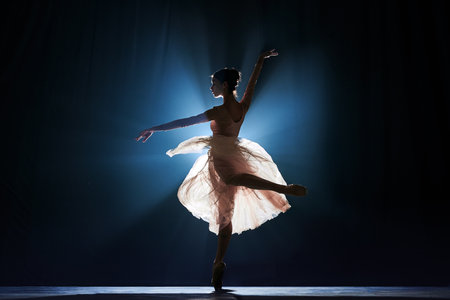 Theatrical performance. Beautiful, tender, graceful ballerina dancing against dark blue background with spotlight. Concept of art, classical ballet, creativity, choreography, beauty, adの写真素材