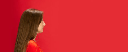 Profile portrait of young beautiful woman looking forward, posing against red studio background. Concept of human emotions, lifestyle, youth, fashion, beauty, business. Copy space for ad, bannerの写真素材