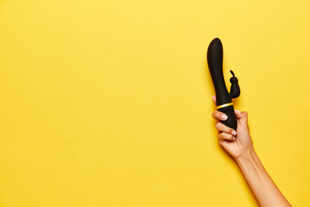 Female hand with vibrator, medical massager over yellow background. Image for sex shop. Concept of...