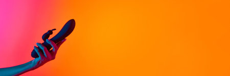 Womans hand holding vibrator, massager over yellow-pink background in neon light. Concept of toys for adult, healthy lifestyle. Copyspace for ad, textの写真素材