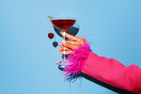 Women hand holding glass with drunk cherry cocktail over blue pop art background. Copy space for ad. Concept of party, relax, alcohol.の写真素材