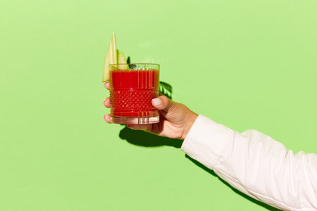 Horizontal photoshoot of female hand holding glass of blood Mary on light green background. Concept of copy space for ad, design, party, relax, pop art.の写真素材