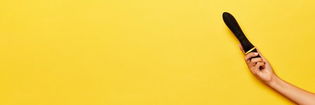 Banner. Female hand with vibrator, medical massager over yellow background. Image for sex shop....