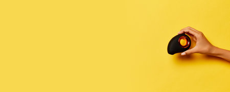 Female hand holding vibrator, medical massager over yellow background. Image for sex shop. Concept...