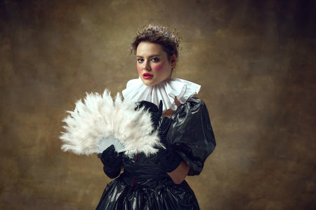 Young dark-haired woman in a ballroom historical black dress made of garbage bags and a fan in her...