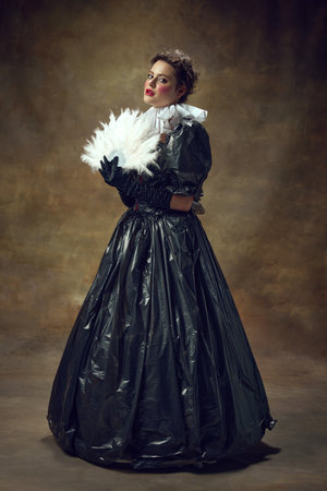Full lenght portrait of woman in ball dress made of garbage bags and fan in hand in vintage room....
