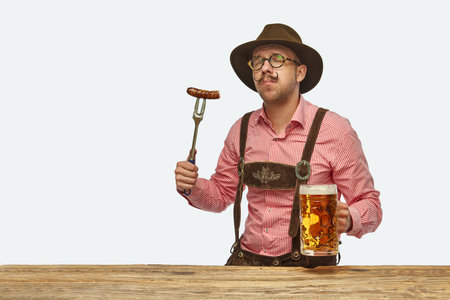 Delightful man wearing traditional fest Bavarian or German outfit with huge beer mug tasting fried sausage.の写真素材