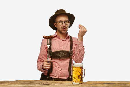 Young man wearing traditional fest Bavarian or German outfit with big beer glass and fried sausageの写真素材