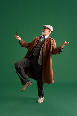 Full lenght photo. Emotional mature man with mustache, dressed in vintage style, looks like detective, laughing while dancing. Concept of fashion, emotions, vintage, retro and adの写真素材