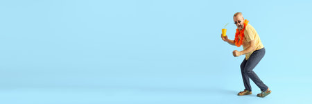 Banner. Middle-aged grey-head man, stylishly, brightly dressed in summer, holds refreshing cocktail dancing with happiness. Concept of emotion, rest, recreation, holidays, vacation. Ad.の写真素材