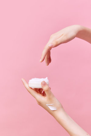 Cropped view of female hands holding jar with cream in hands. Using cosmetics product isolated pastel pink background. Concept of body and skin care, spa, dermatology. Copy space for adの写真素材