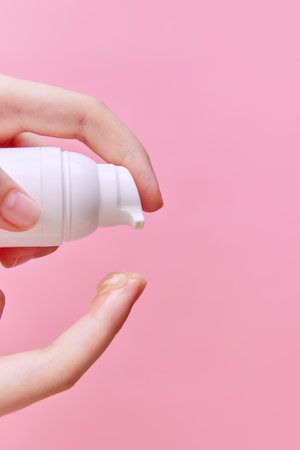 Close up image of female hand squeezing cream, gel for hands from unmarked bottle with dispenser on finger on pastel pink background. Concept of body and skin care, spa, dermatology. Copy space for adの写真素材