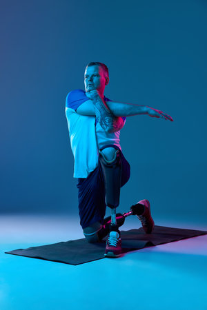 Confident man in sport uniform prosthetic legs doing exercises, stretching hands in neon light....