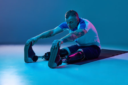 Confident man in sport uniform prosthetic legs doing stretching exercises on floor in neon light....