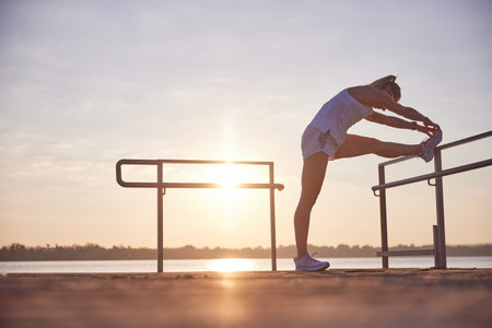 Young woman doing warming-up training near seaside. Morning fitness exercise on beach, near ocean on...