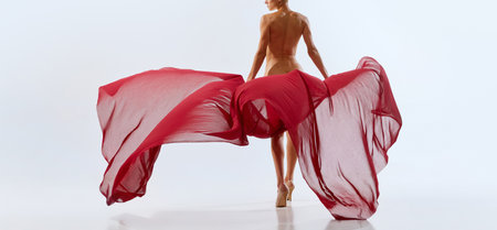Cropped back view portrait of young nudity woman body, buttocks with bright red floating freely fabric over studio background. Ad. Concept of natural beauty of body, feminine energy, cosmetology.の写真素材