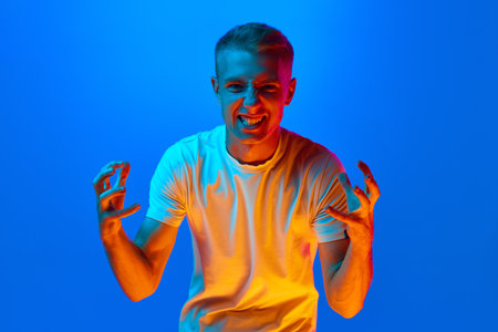 Portrait of young agressive, angry, irritated man, student in white t-shirt looking at camera...