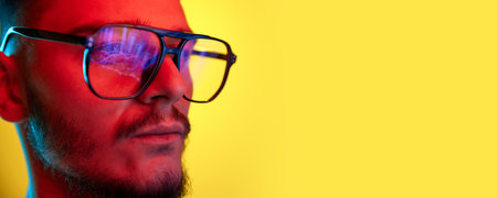 Close Up side view portrait of young handsome guy, student in glasses reflects scoring, rates, graphs isolated on yellow background in red neon light, filter. Concept of youth, beauty. Banner. Posterの写真素材