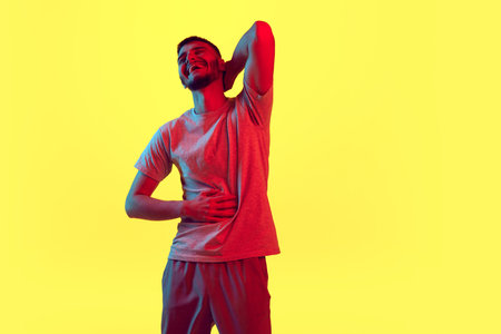 Portrait of laughing, smiling young man, student in casual outfit isolated on yellow background in...