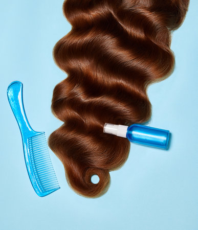 Photo of wavy long brunette hair, spray, comb against blue background. top view, flat lay. copy space. Self care, hair treatment. Natural beauty, organic cosmetic, care product concept. adの写真素材