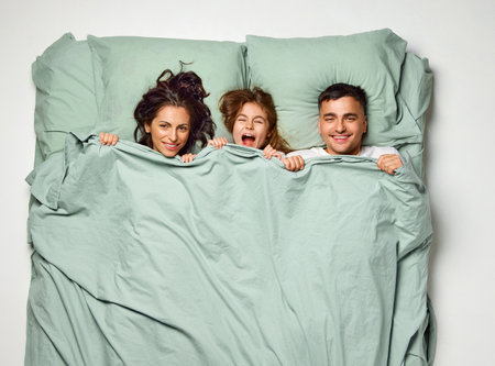 Top view portrait of smiling, laughing people in bed. Cute child lying, having fun with parents in one bed with mint bedding. Enjoying being together. Concept of sleep wellness, family time, love.の写真素材