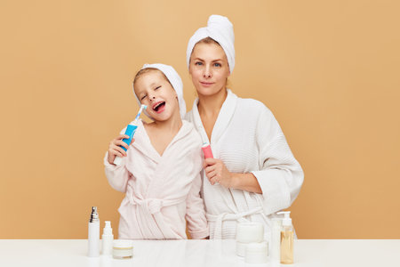 Portrait of lovely mother with daughter holding tooth brush near beauty table with cosmetic and hygiene products. Woman and kid together care of beauty, health. Concept of beauty, spa, wellness.の写真素材