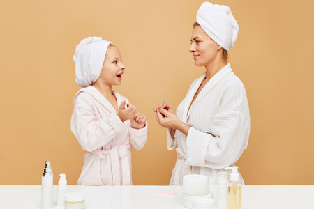 Side view portrait of mother and daughter filing nails in bathroom over beige backgrounds. Woman and kid together care of beauty, health. Concept of spa, wellness, pedicure, manicure, hygiene. adの写真素材