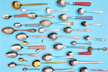 Cutlery. Flat lay photo of variety of antique silverware and gold kitchen spoons arranged against blue studio background. Concept of food, holiday, table setting, retro, vintage. copy spaceの写真素材