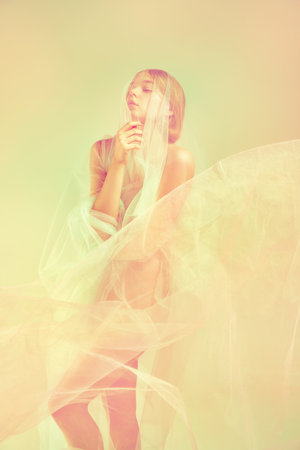 Young beautiful woman with closed eyes standing alone covered transparent fabric. Retro pastel color palette. Natural beauty of female body concept. Highlights effectの写真素材