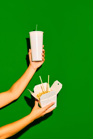 Take it away. Close up image of hands holds one opened paper box with noodles and refreshing drink...