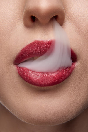 Cropped photo. Extreme close up of woman with red lips blowing smoke from mouth. Bad habits. No...