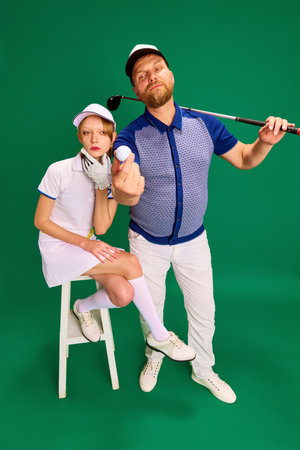 Top view. Father and daughter on golf court. Dad, man and girl, teenager dressed like golf players posing on green background. Concept of parenthood, hobby, recreation, healthy and active lifestyle.の写真素材
