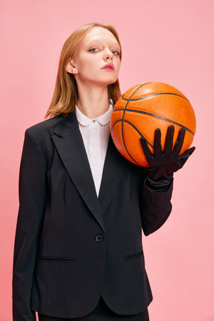 Half length portrait of young pretty woman dressed smart casual outfit in elegant gloves holding basketball ball isolated pastel pink background. Concept of active lifestyle, business, sport, hobby.の写真素材
