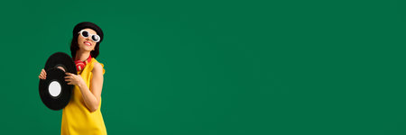 Banner. Pretty woman wearing fashion look with sunglasses and hat holds retro music plates and dancing isolated bright green studio background. Concept of fashion, style, human emotions. Copy spaceの写真素材