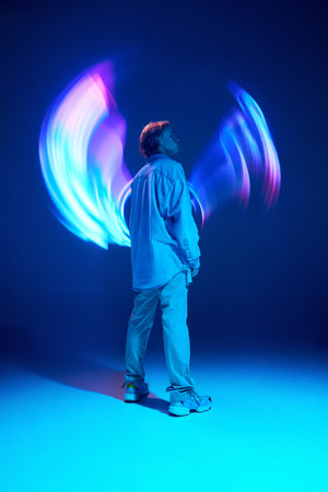 Full-length rear view portrait of attractive young man posing in vivid blue neon light illuminating...
