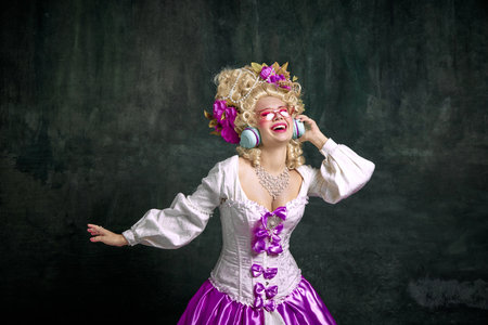 Happy overjoyed woman in old-fashioned dress with corset and hairstyle dancing while listening music...