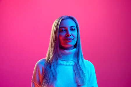 Close up portrait of young attractive calm woman in knitted warm sweater against pink background in neon light. Concept of beauty, human emotions, facial expression, fashion and style.の写真素材
