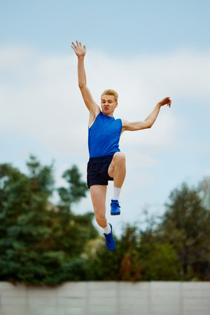 leap of determination frozen in this captivating long jump photo. motivated young man, professional sportsman doing perfect jump. Concept of kinds of sport, championship, motivation, energy.の写真素材