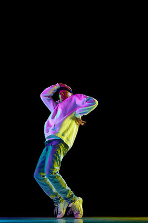 Young stylish man, break dancing dancer practicing solo in casual outfit against black background in...