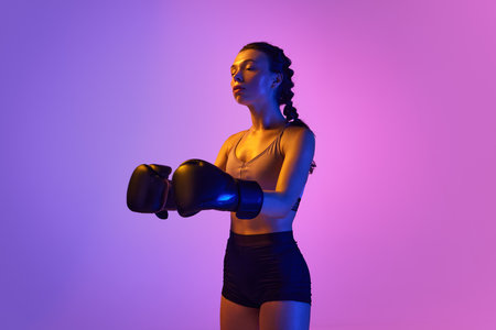 Intense and captivating, a professional boxer girl stands out against gradient pink-violet studio background in neon light. Concept of sport, active lifestyle, health, competition, championship.の写真素材