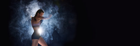Banner. Flyer. Focused and powerful, female sportsman gearing up for battle, against black studio background in stage smoke. Negative space for text. Concept of sport, active lifestyle, competition.の写真素材