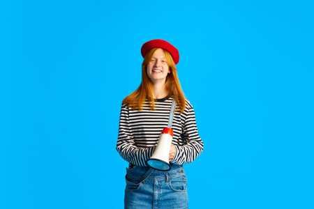 Happy cheerful young lady in red beret, looks like Frenchwoman and posing with loudspeaker in hand...