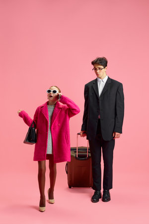 Schoolgirl dressed in lady boss outfit talking on phone while she going to business travel with her personal assistant against pink studio background. Concept of business, office, work, management.の写真素材