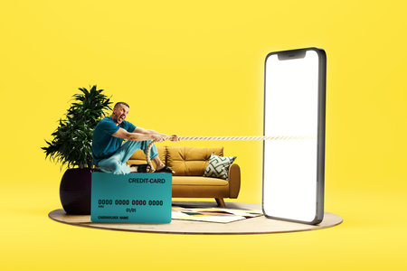 Emotional man sitting on credit card and pulling robe from giant 3D model of mobile phone with empty...