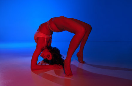 Elegance and neon vibrancy. Young naked woman posing , stands in bridge pose in underwear against...