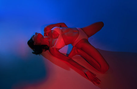 Elegance and neon vibrancy. Young woman posing in underwear against studio background in energetic glow of neon light. Concept of art, female health, wellness, self-expression.の写真素材