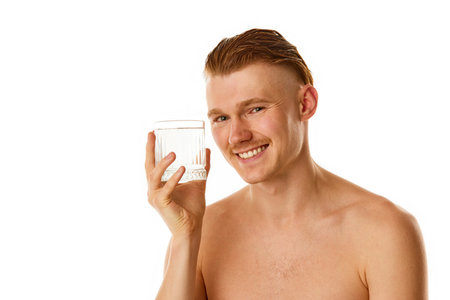 water balance. Attractive smiling redhaired, ginger man holding glass full of water against white studio background. Concept of natural beauty, selfcare, body and skincare, health, hygiene, fashion.の写真素材